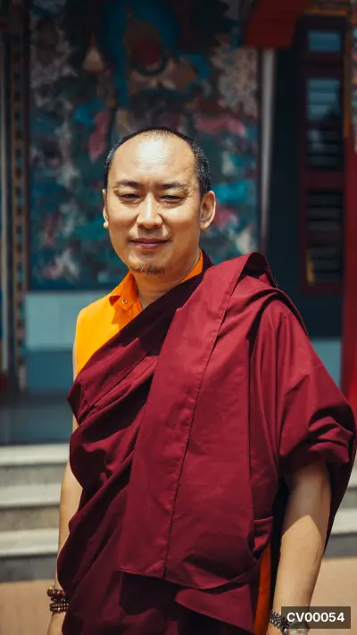 Vị tỳ kheo Tây Tạng mặc áo cà-sa đỏ rượu, đứng trước bức tranh thangka nhiều màu sắc