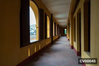 Hành lang có tường màu vàng, cổng vòm, cửa chớp gỗ nâu và sàn gạch đỏ