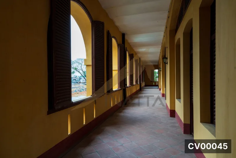 Hành lang có tường màu vàng, cổng vòm, cửa chớp gỗ nâu và sàn gạch đỏ